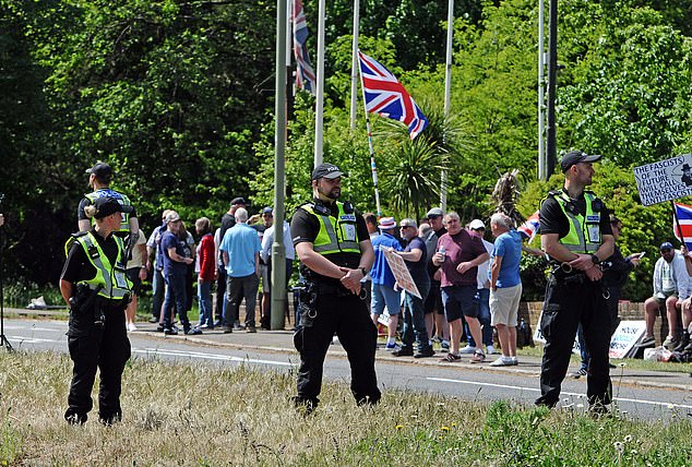 Police stand on guard as both groups protest outside the site housing asylum seekers earlier today