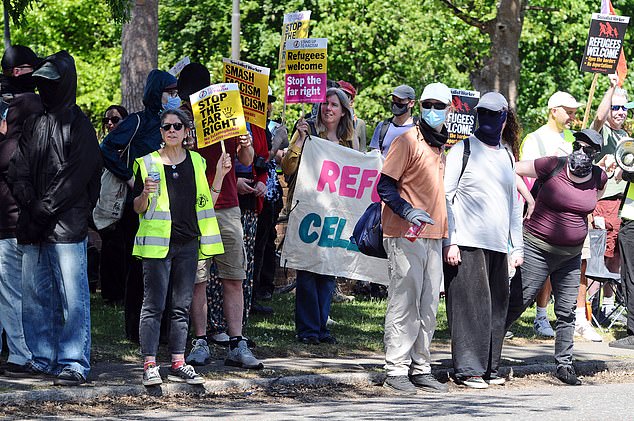 Pictured: Pro-migrant protesters chanting on the side of the road near the hotel earlier today
