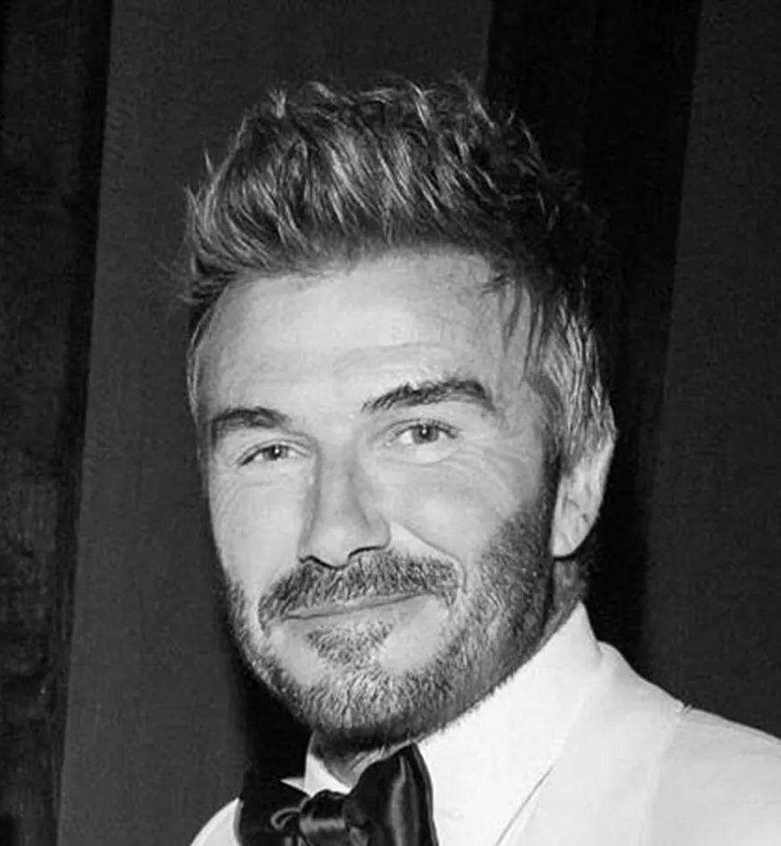 Black and white photo of David Beckham with two other men in tuxedos at his 50th birthday party.