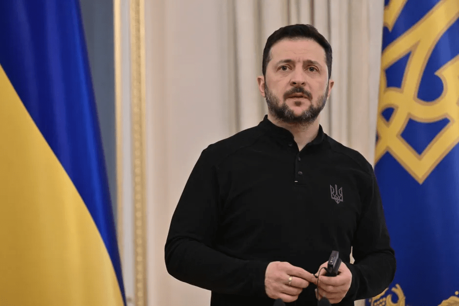 Volodymyr Zelenskyy in front of Ukrainian flags.
