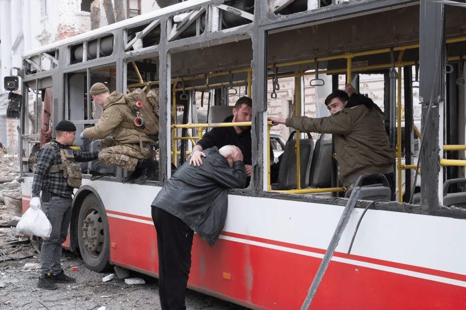 Soldiers assisting an elderly man from a damaged bus.