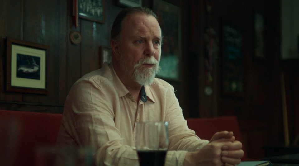 A man sits at a table in a pub, looking pensive.