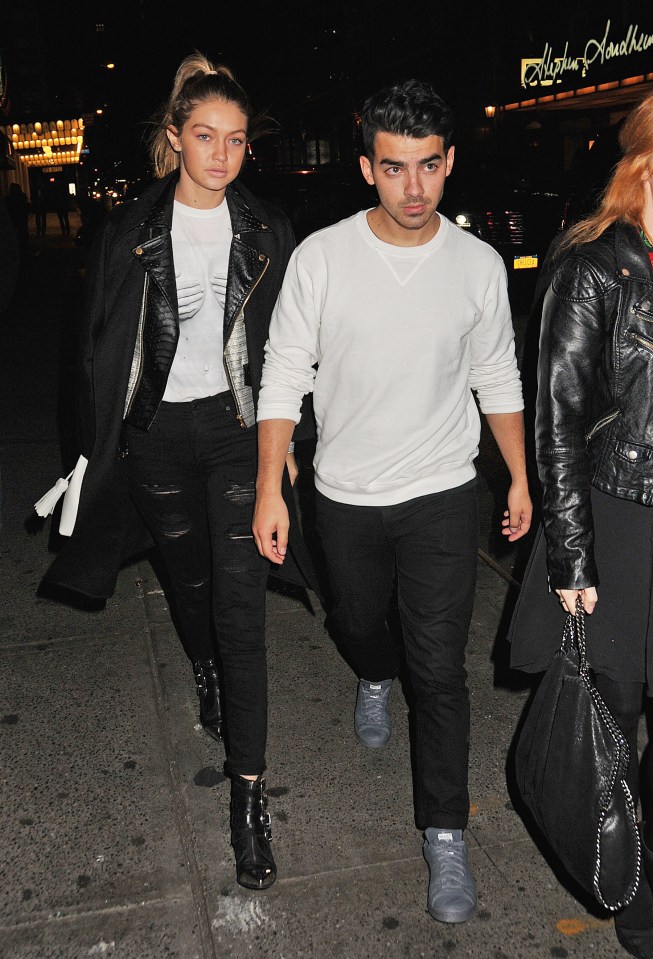 Gigi Hadid and Joe Jonas walking down a city street at night.