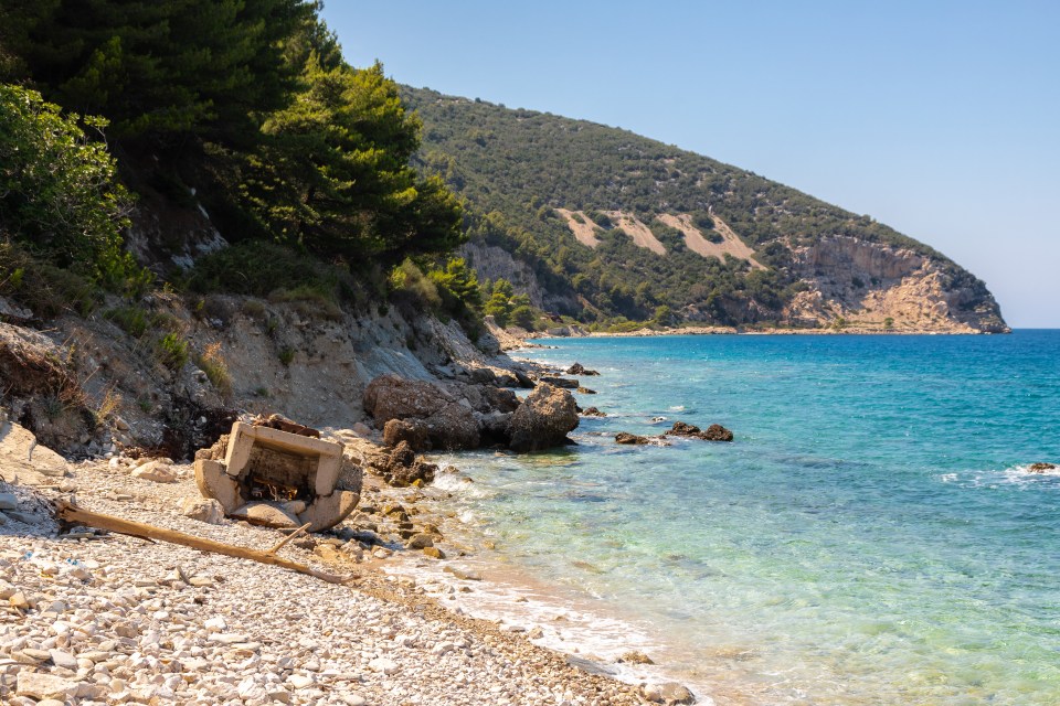 Rocky beach on Sazan Island, Albania, with clear turquoise water and remnants of a concrete structure.