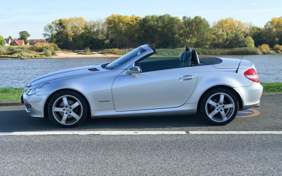 Silver Mercedes SLK convertible parked by a body of water.