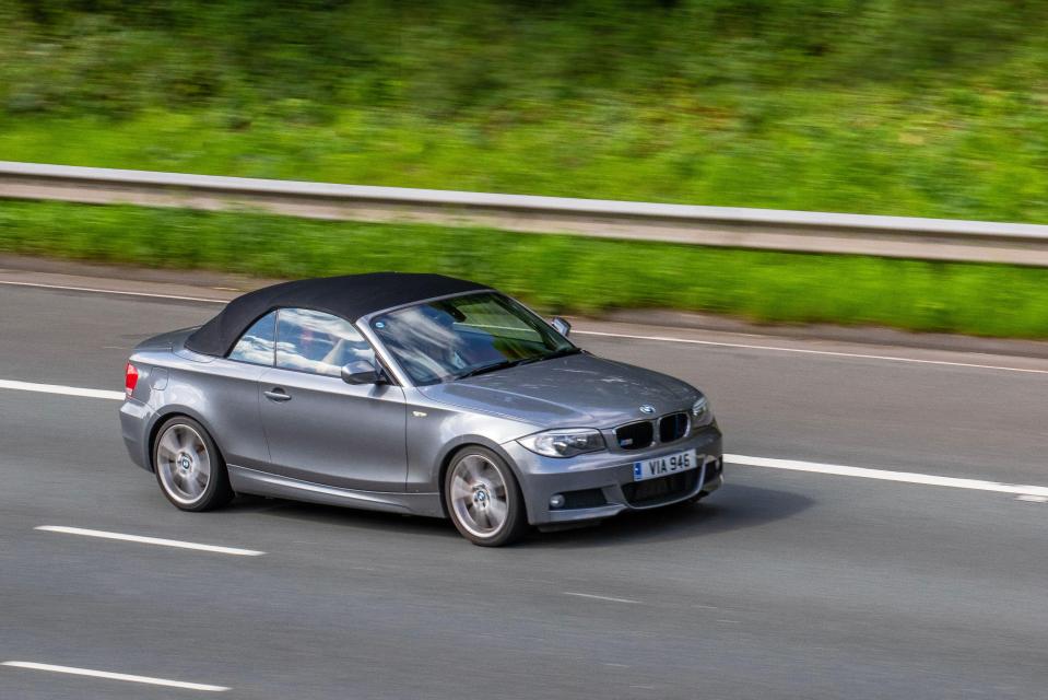 Grey BMW 1 Series convertible driving on a highway.