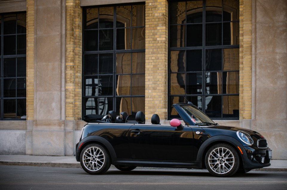 Black Mini Cooper S convertible parked in front of a brick building.