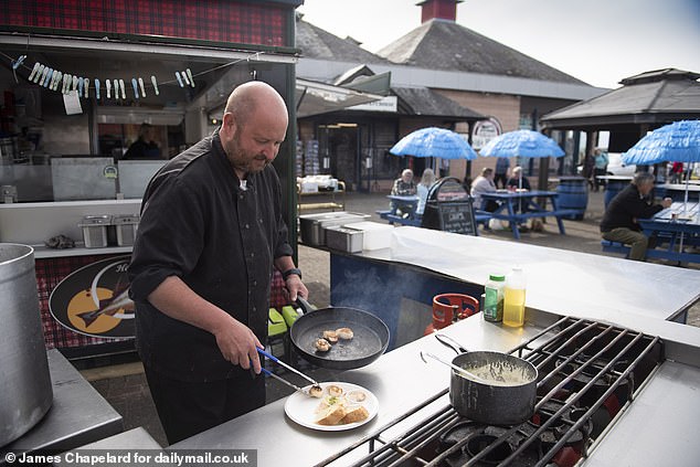 His bustling tartan stand is situated on right by the shore, drawing in hungry visitors with the inviting aroma of the seafood caught fresh every morning, such as scallops, prawns and mussels, being grilled by his chef