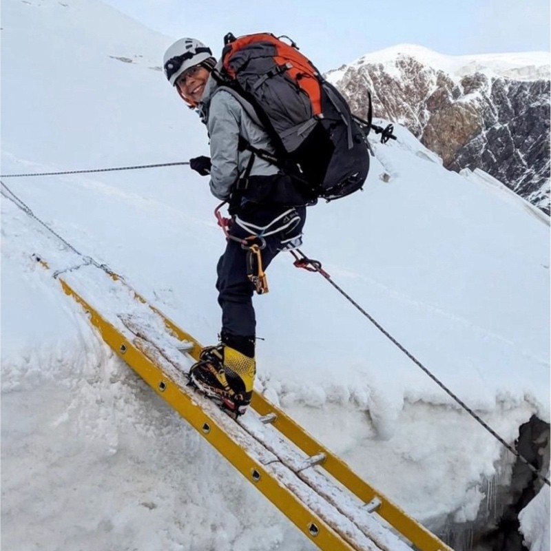 Climber ascending a snowy mountain using a ladder.