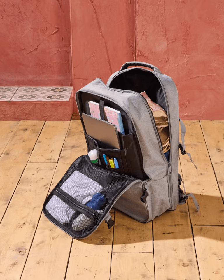 Grey backpack open, showing its contents: laptop, notebooks, clothes, and other items.