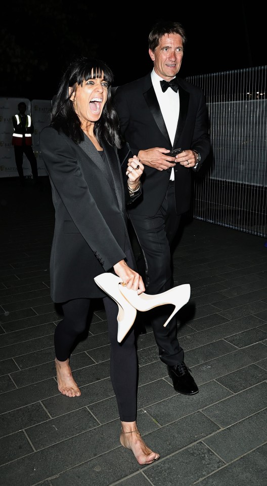 Claudia Winkleman and a man in formal wear leaving the BAFTA TV awards, she is barefoot and holding her shoes.