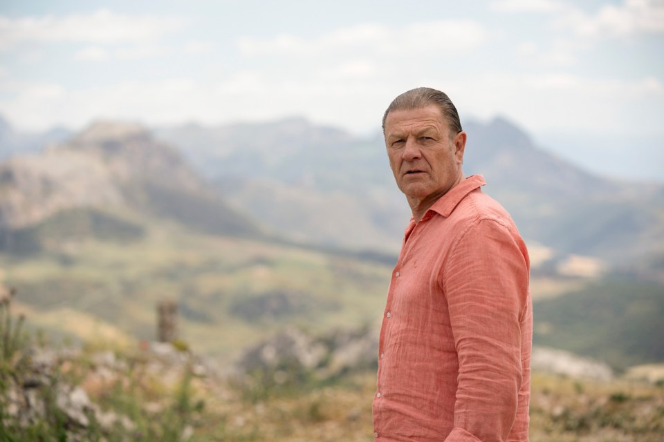 Sean Bean standing in a mountainous landscape.