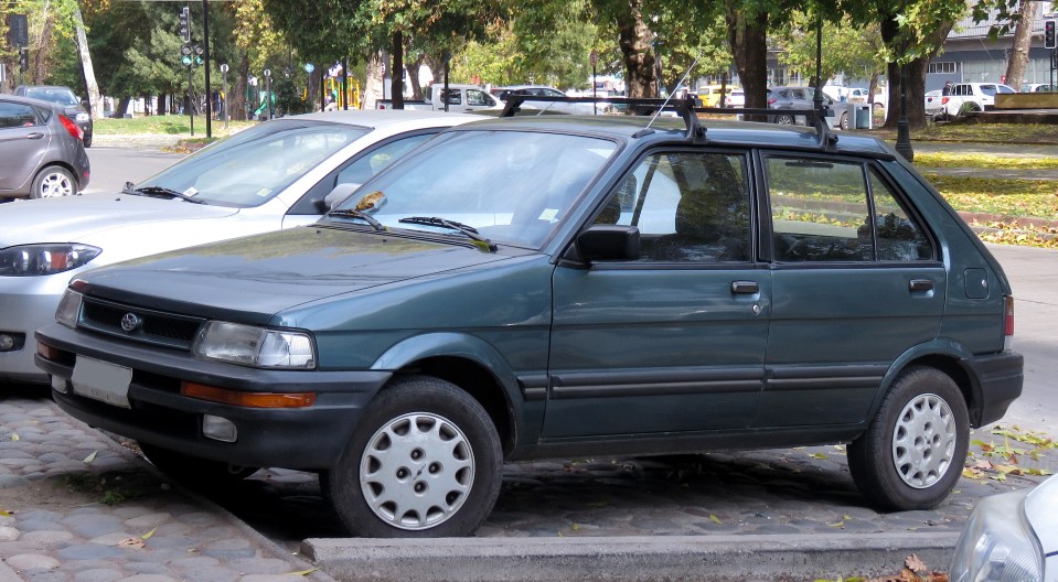 A dark-green Subaru Justy hatchback parked on a cobblestone street.