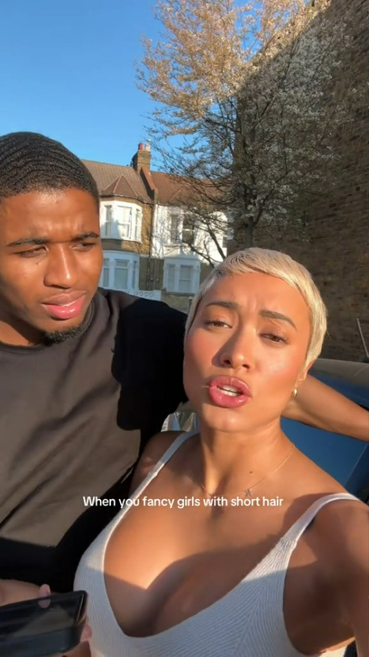 A woman with short blonde hair and a man stand outside on a sunny day.