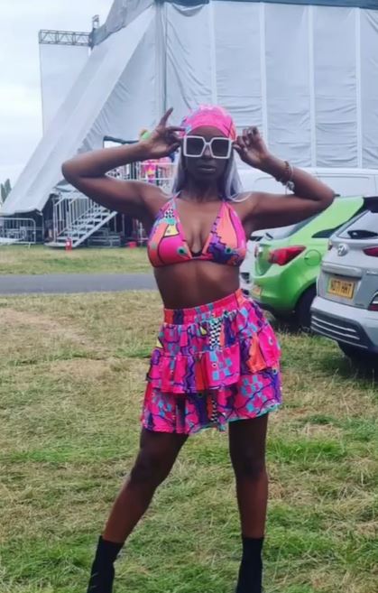 Woman in pink patterned bikini and skirt, wearing sunglasses and headscarf.