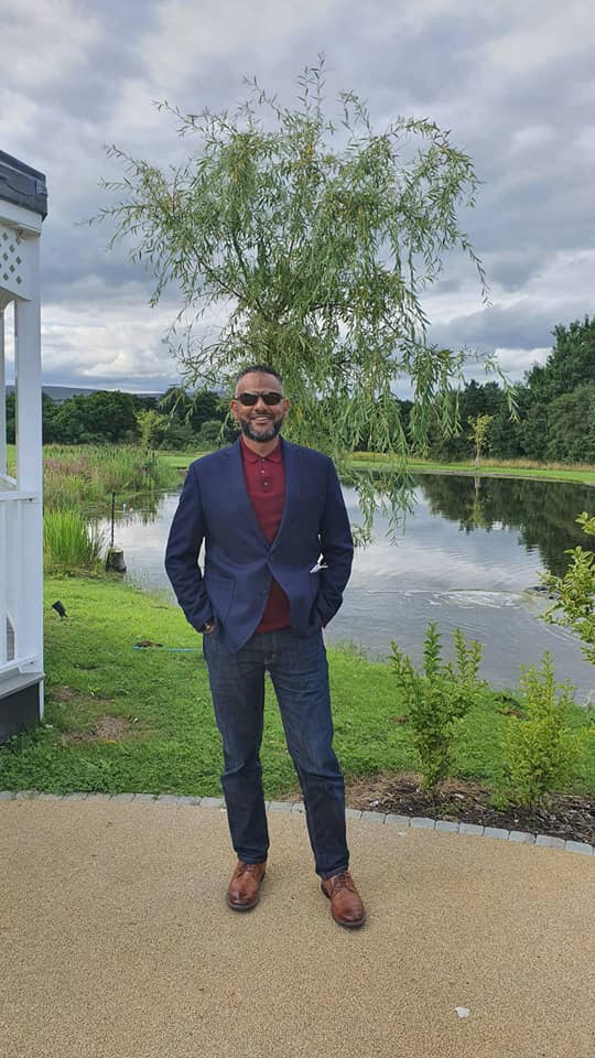 Man in suit standing outdoors by a pond.