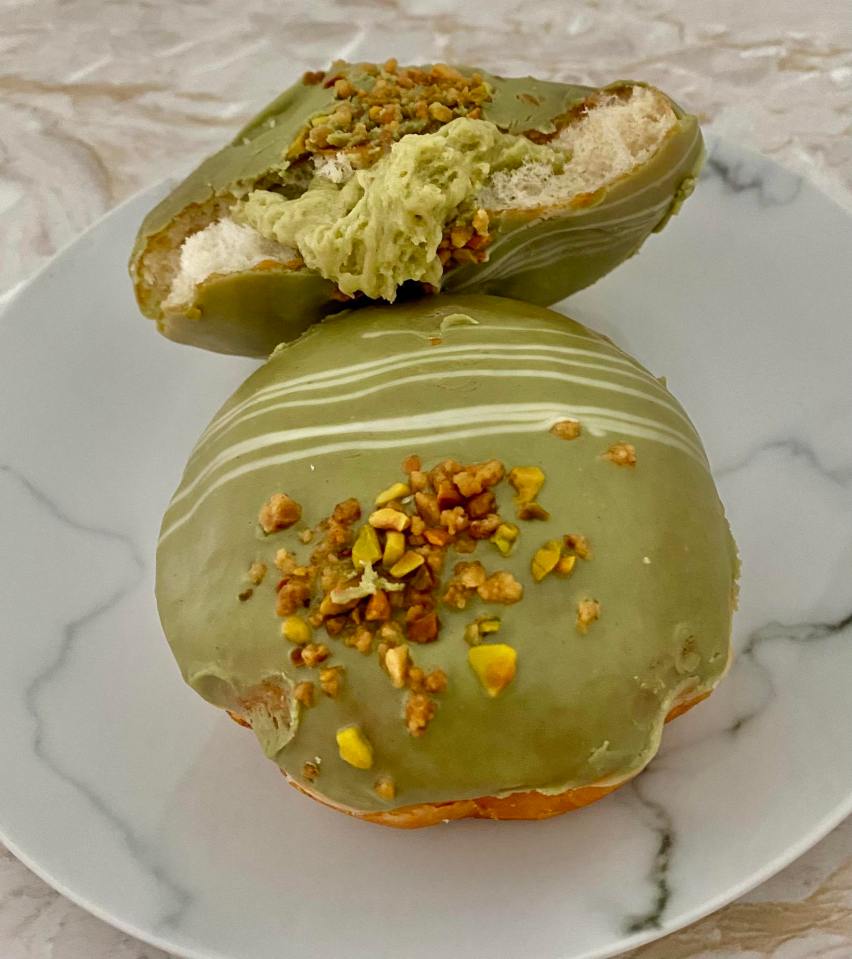 Two pistachio-flavored doughnuts with white chocolate drizzle and pistachio nibs.
