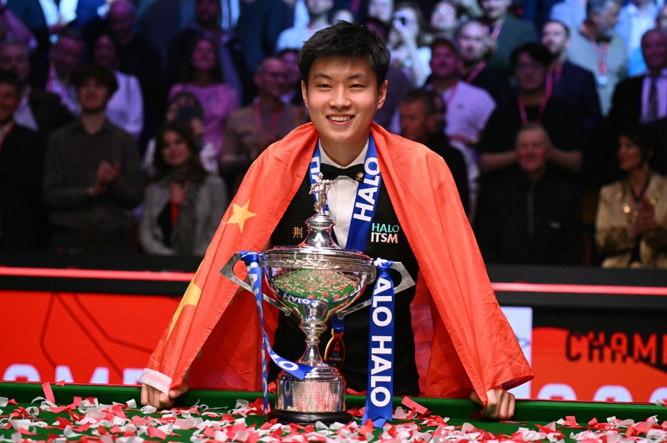 Zhao Xintong, draped in a Chinese flag, poses with the World Snooker Championship trophy.