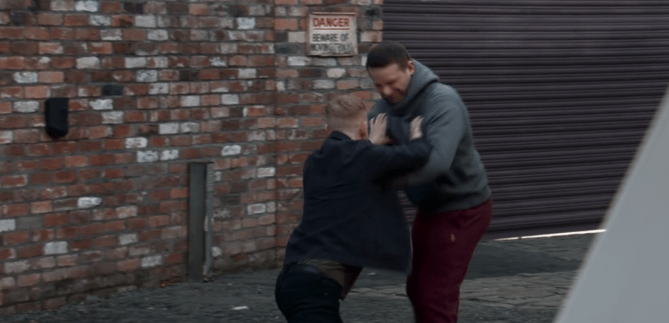 Two men grappling in a brick alleyway.
