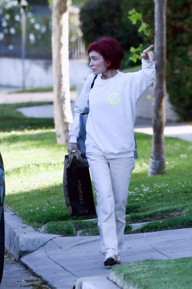 Sharon Osbourne walking down a sidewalk, carrying a shopping bag.