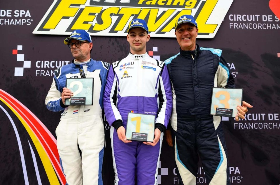 Three race car drivers on a podium holding their trophies.