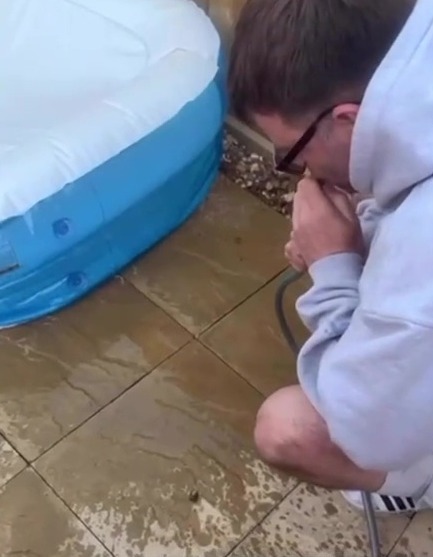 Person siphoning water from a paddling pool using a hose.