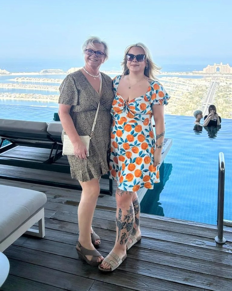 Two women in dresses stand by an infinity pool overlooking a city.