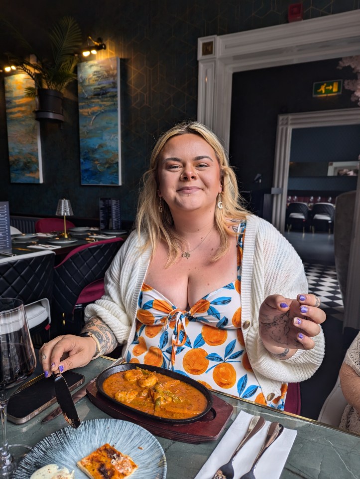 Woman smiling at restaurant, eating shrimp dish.