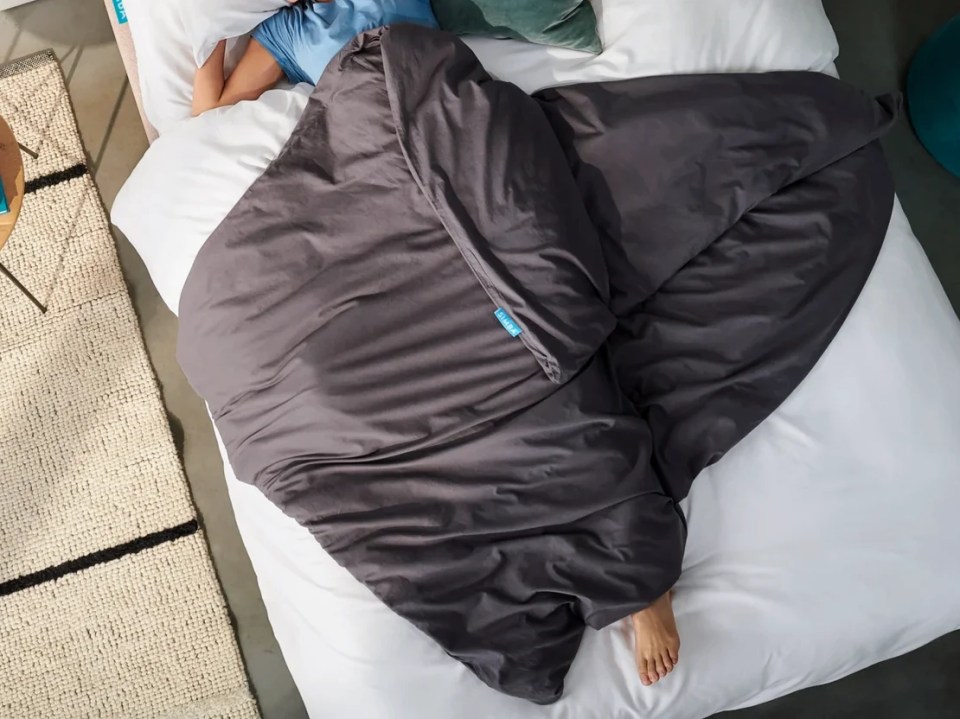 Person sleeping under a gray weighted blanket.
