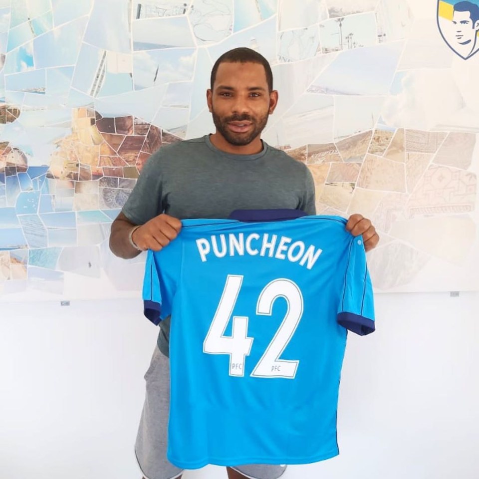 Man holding up a light blue soccer jersey with "Puncheon 42" on the back.