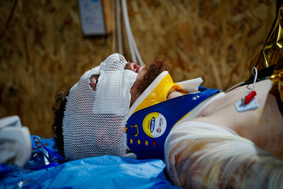A wounded soldier in a neck brace and bandages awaits an ambulance.