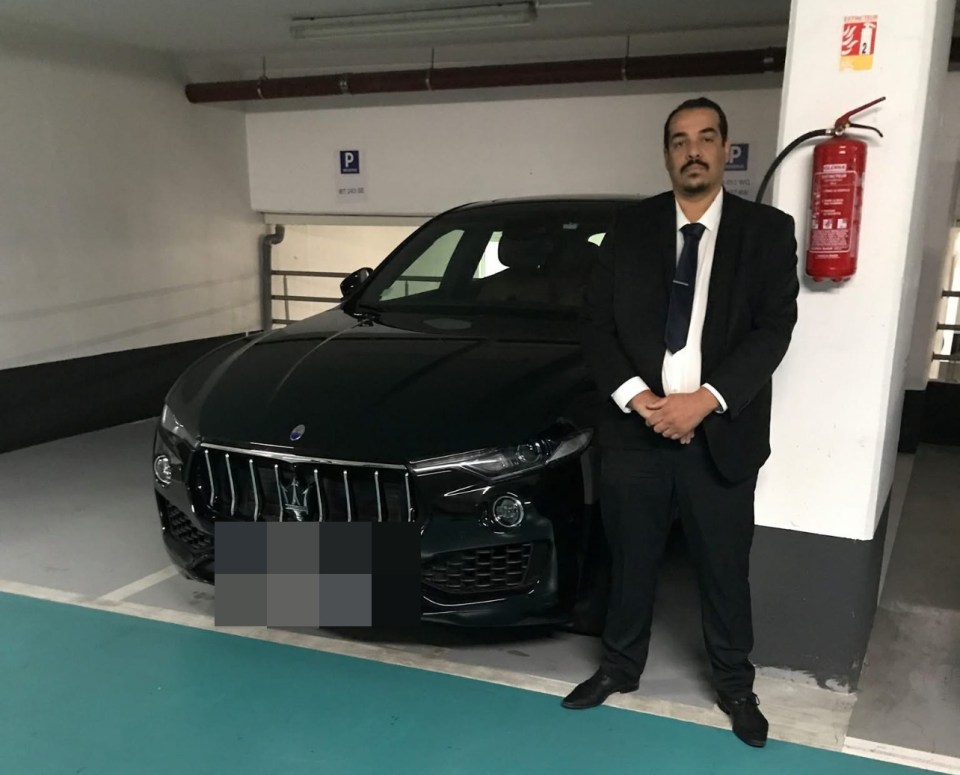 A man in a suit stands next to a black SUV in a parking garage.