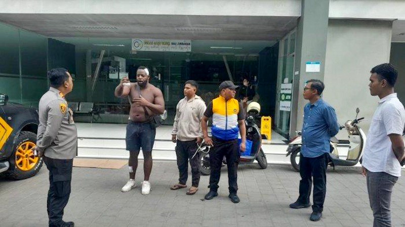A British tourist, injured and shirtless, speaks with police officers in Bali after a road rage incident.