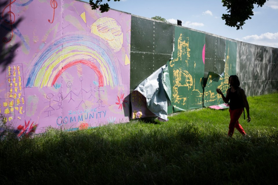 Person walking past a damaged festival screen with children's drawings.
