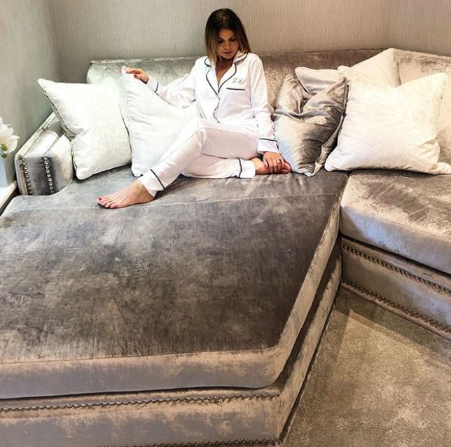 Woman in pajamas relaxing on a large gray velvet sectional sofa.