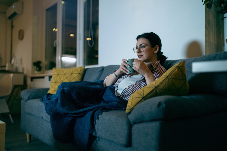 Woman relaxing on a couch, drinking tea and watching TV.