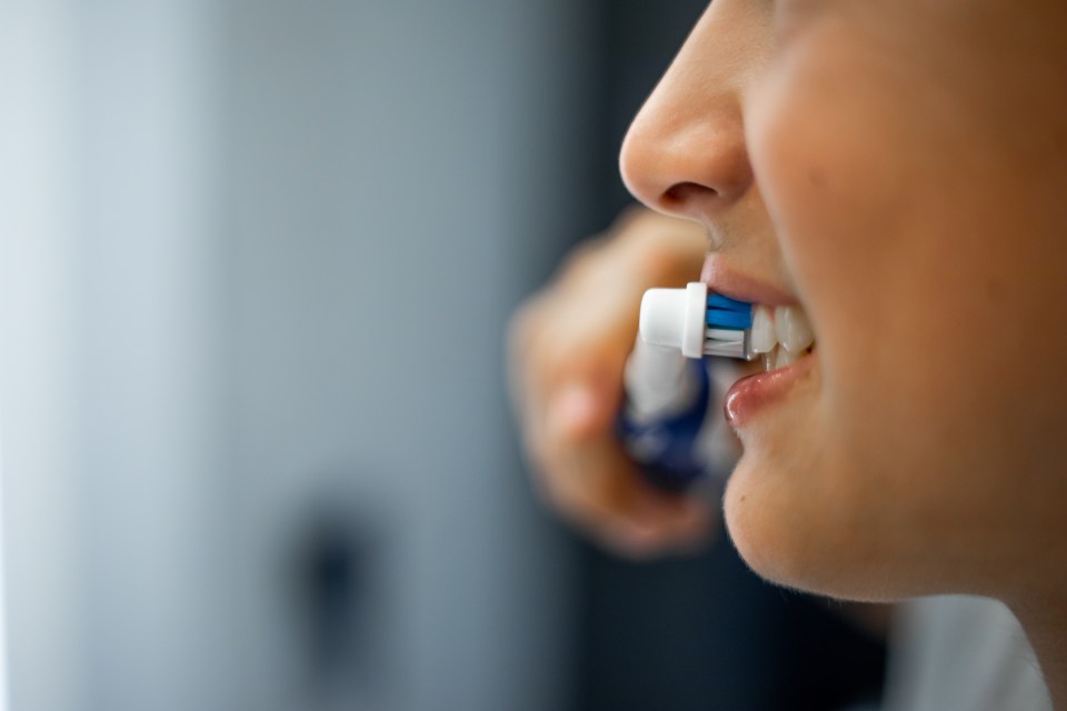 Teenage boy brushing his teeth with an electric toothbrush.