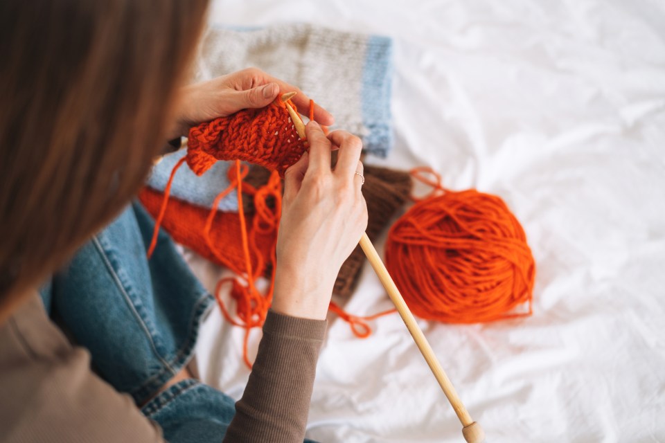 Woman knitting with orange yarn.