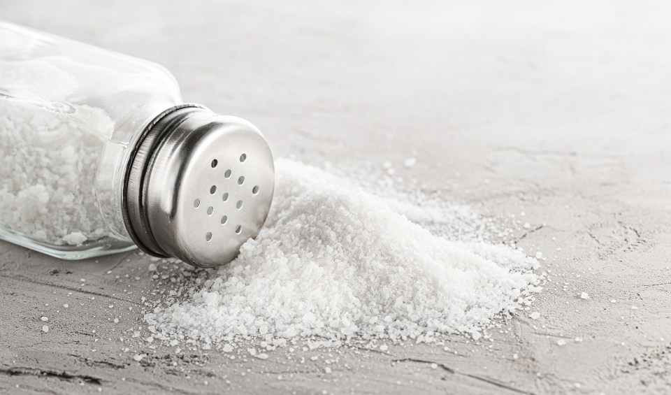 Spilled salt next to a salt shaker.