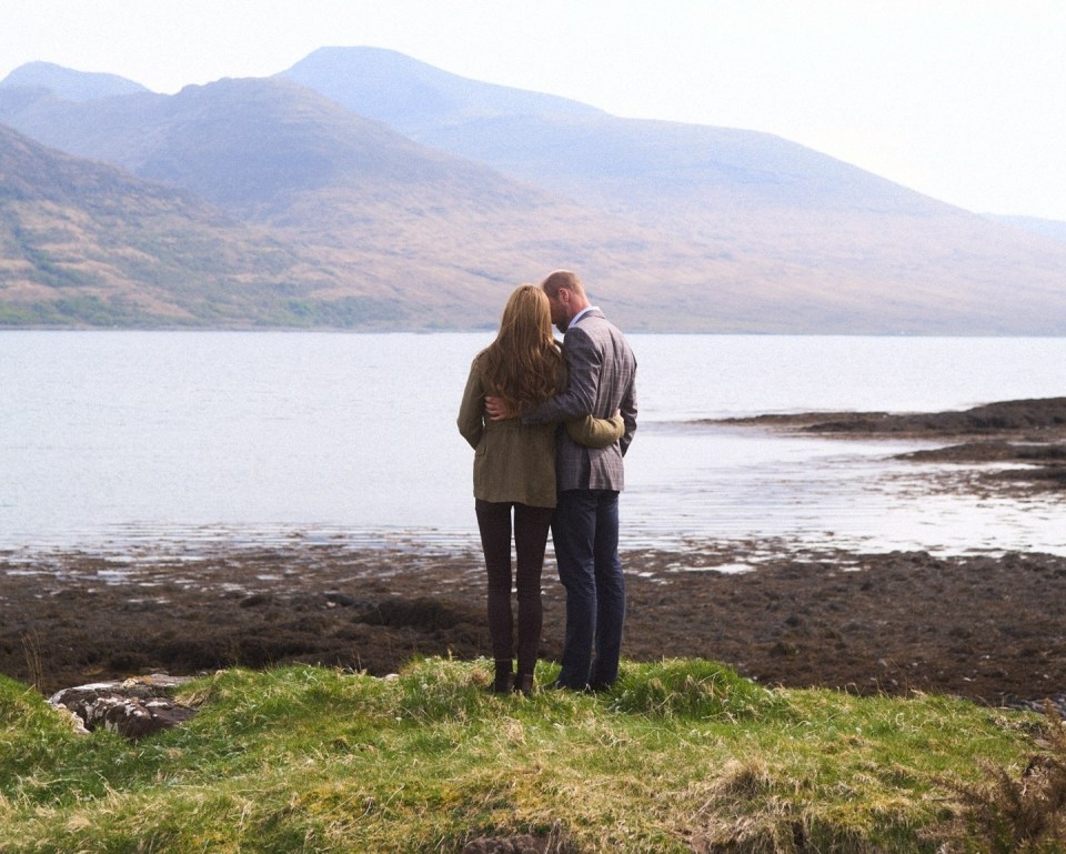 The Prince and Princess of Wales embracing overlooking a loch and mountains.