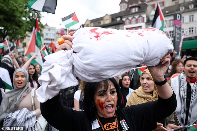 A demonstrator, with fake blood smeared on her face, holds a prop, which is said to represent a body bag in the air