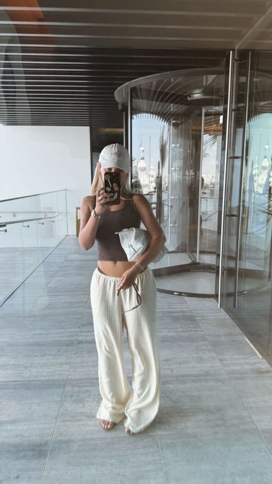 Woman taking a selfie in a white cap and striped pants.