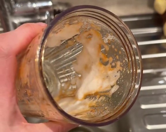 A hand holding a stained blender cup over a sink.