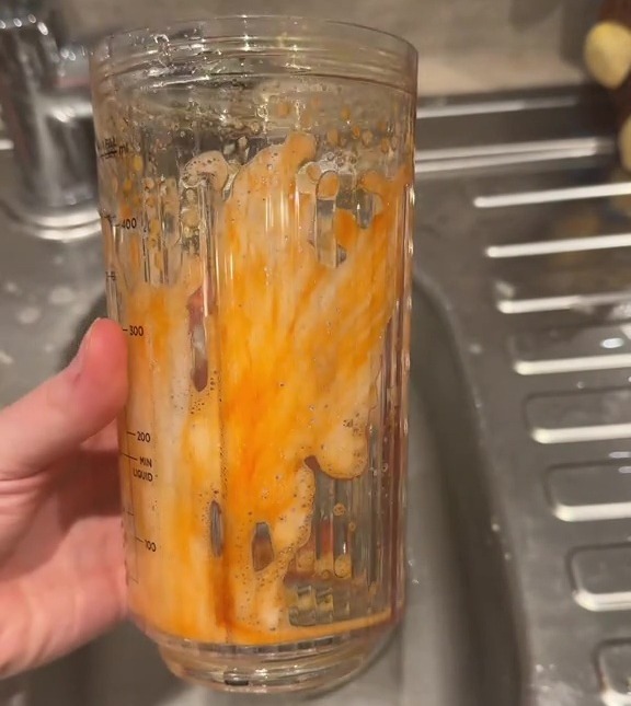 A hand holding a stained blender cup in a sink.