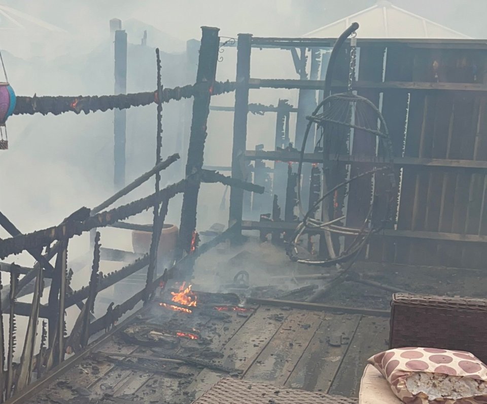 Fire-damaged garden with smoldering debris and a burned patio chair.