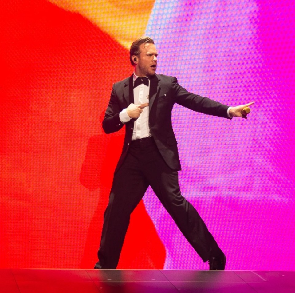 Olly Murs performing on stage with a large screen displaying a stylized image of himself.