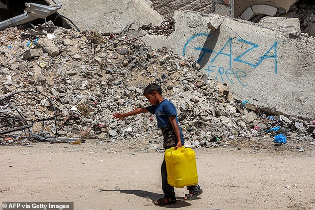 A boy walks carrying a jerrycan filled with water past the rubble of a destroyed building in Gaza City on April 21, 2025