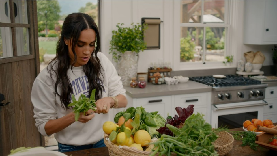 Meghan Markle preparing herbs and produce in a kitchen.
