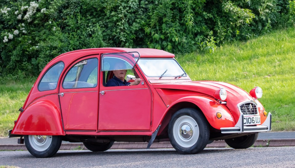 A red 1986 Citroën 2CV driving down a road.
