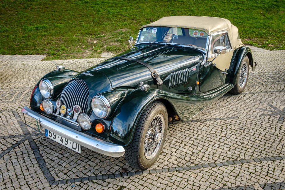 Dark green Morgan 4-4 sports car parked on cobblestones.